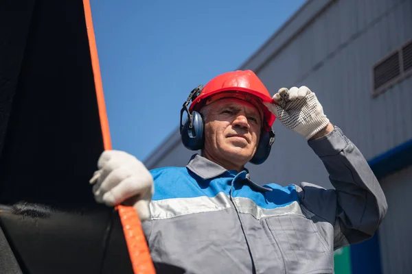 Bulldozer conductor mina de carbón en uniforme con casco y auriculares mirando a un lado. Concepto hombre retrato industrial Imagen de archivo