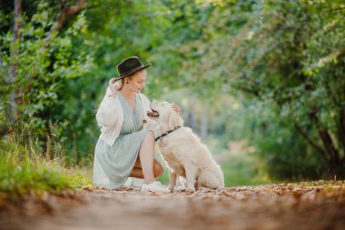 Şapkası ve golden retriever 'ı olan bir arkadaşlık kızı düşün. Arka plandaki yaz parkında köpeği olan güzel genç bir kadın.