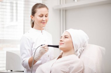 Yüzü kaldırmak için elektrotlarla mikro akım galvanik yüz tedavisi gören genç bir kadın. Sivilce ve yağlı cilt sorunlarını önleme kavramı