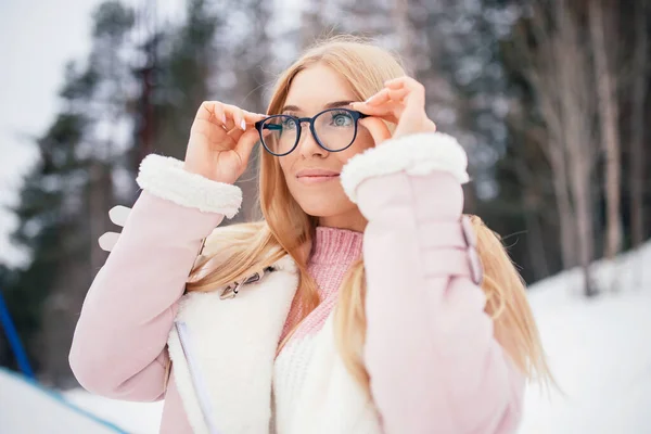 Χειμερινό πορτρέτο μόδας των νέων ευτυχισμένη ξανθιά γυναίκα κρατώντας γυαλιά για την όραση στο φόντο του δάσους και του χιονιού — Φωτογραφία Αρχείου