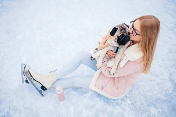 Молодая женщина занимается зимними видами спорта на катке с собакой-мопсом — стоковое фото