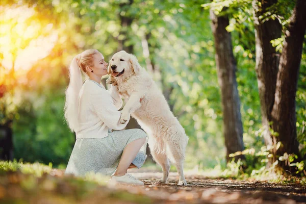 Jovem atraente com golden retriever. Menina abraços cão labrador fundo verão parque. Conceito companheiro amizade animal e pessoas — Fotografia de Stock