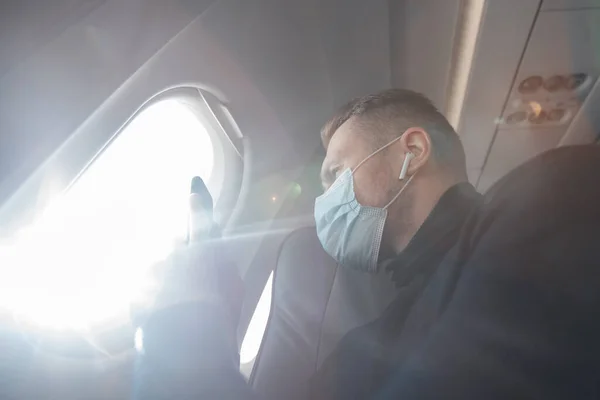 Man med säker mask passagerare i flygplan använda mobiltelefon för foto i stolen. Begreppsresa — Stockfoto