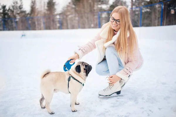 Hermosa chica con perro pug en pista de patinaje en invierno, jugando deportes junto con los animales Fotos de stock libres de derechos
