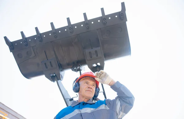 Motorista de escavadeira em estandes de chapéu duro em equipamentos de construção, conceito retrato homem industrial Imagem De Stock