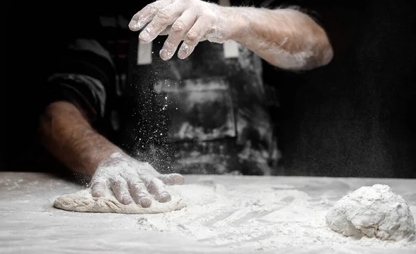 Manos panadero preparación de masa de levadura con harina de polvo blanco sobre fondo negro, cucharada de pasta y pizza — Foto de Stock