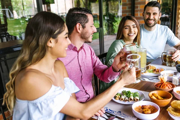 Group of Young latin Friends Meeting For beer, michelada Drinks And mexican Food Making A Toast In Restaurant terrace in Mexico Latin America