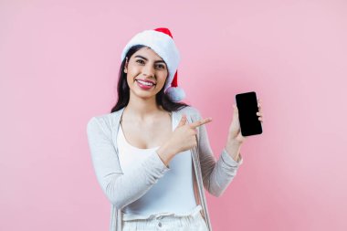 Pembe arka planda bir noel konseptinde cep telefonlu genç Latin kadının portresi