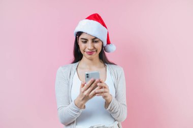 Pembe arka planda bir noel konseptinde cep telefonlu genç Latin kadının portresi
