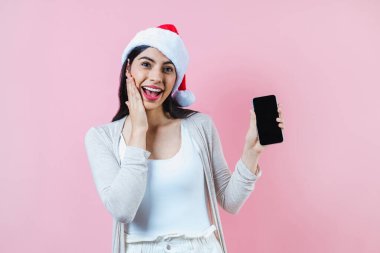 Pembe arka planda bir noel konseptinde cep telefonlu genç Latin kadının portresi