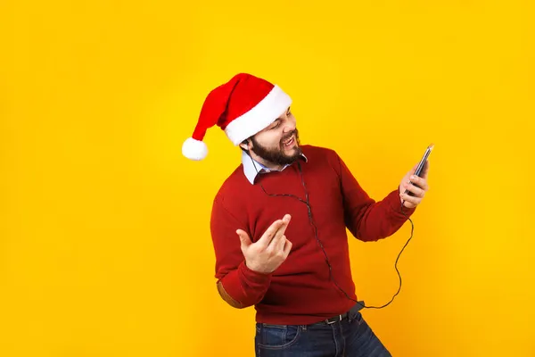 拉汀男子在圣诞节的概念听音乐与耳机和手机与桑塔帽子在黄色的背景在墨西哥拉丁美洲 — 图库照片