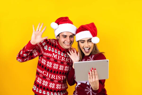 若いラテン系のカップルは黄色の背景にデジタルタブレットやタッチパッドを使ってクリスマスビデオ通話をしています — ストック写真