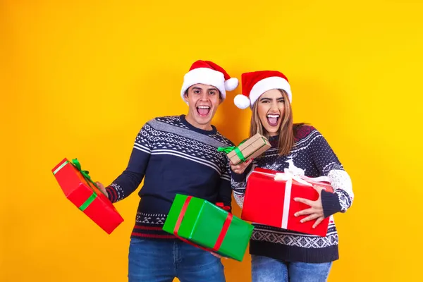 ラテンカップルの友人男性と女性で赤クリスマスセーターとサンタ帽子保持プレゼントボックス上の黄色の背景にメキシコラテンアメリカ — ストック写真
