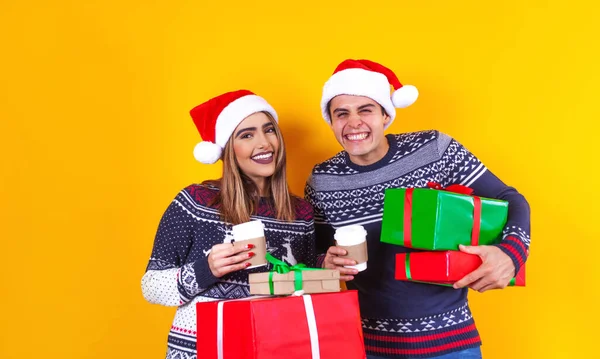 若いですラテンカップル友人男性と女性で赤いセータークリスマスは帽子を保持現在のボックスでギフトリボン弓でメキシコで黄色の背景ラテンアメリカ — ストック写真