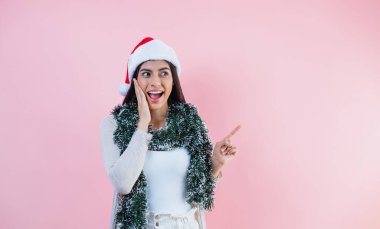 Genç Latin bir kadının portresi pembe arka planda bir noel konseptinde boşluğu işaret ediyor.