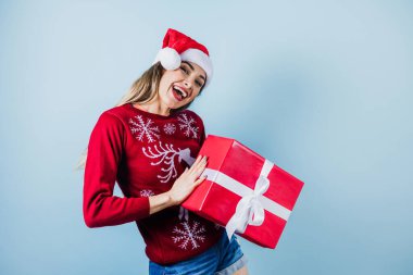 Latin Amerika 'da genç bir kadın Noel hediyelerini mavi arka planda, Noel şapkasıyla tutuyor.
