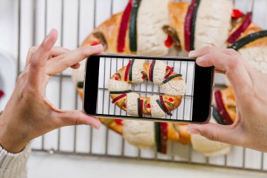 Meksikalı bir kadın geleneksel Rosca de Reyes ya da epifani pastası pişiriyor ve Meksika Latin Amerika 'da Krallar Günü için mutfakta cep telefonuyla fotoğraf çekiyor.