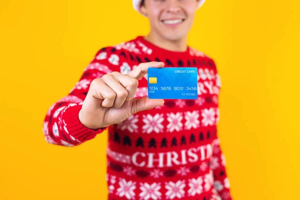 图片说明墨西哥拉丁裔男子持信用卡在圣诞节购物 戴着一顶黄色背景的圣塔帽 — 图库照片