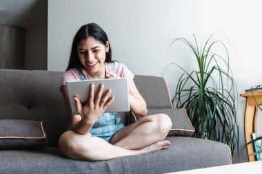 Meksika 'da evdeki kanepede otururken dijital tablet kullanan genç Latin kız öğrenci. 