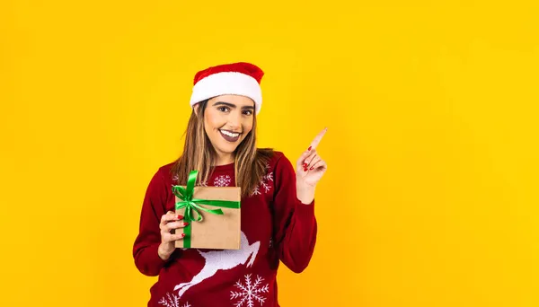 young latin woman holding christmas presents in christmas hat on yellow background in Mexico Latin America