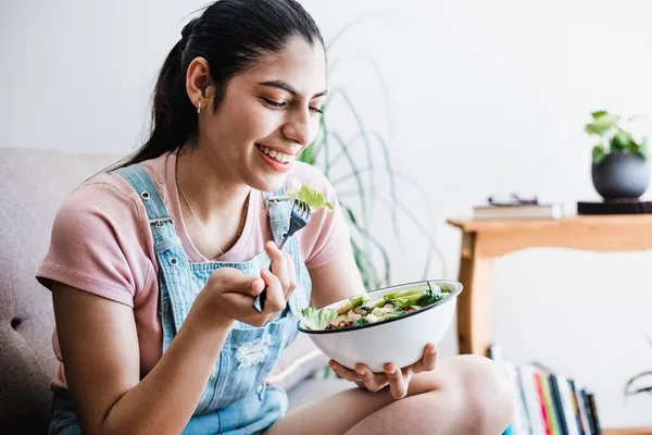 young latin woman eating vegetable or salad bowl, healthy food at home in Mexico Latin America