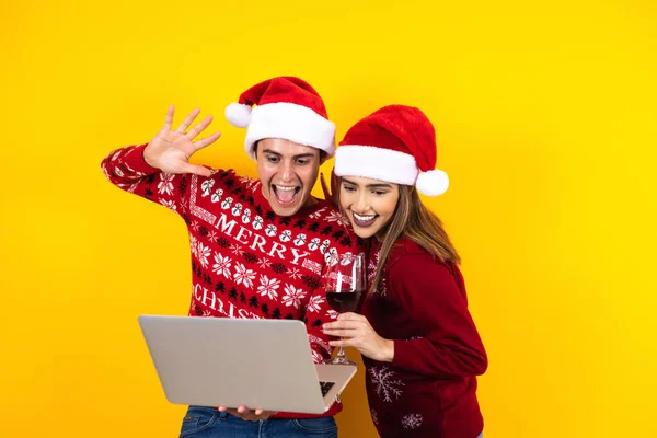 若いラテン系のカップルは黄色の背景にデジタルタブレットやタッチパッドを使ってクリスマスビデオ通話をしています — ストック写真