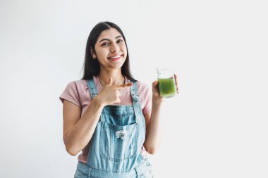happy young latin woman holding bottle of green juice on white background in Latin America clipart