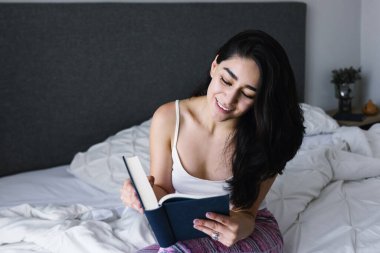 Latin kökenli genç bir kadın kitap okuyor ve Meksika Latin Amerika 'da yatağında okuyor.
