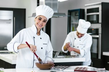 Latin kadın pasta şefi üniforma giyiyor, elinde bir kase tutuyor Meksika 'da mutfakta lezzetli çikolatalar hazırlıyor.