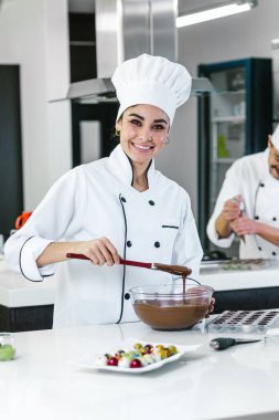 Latin kadın pasta şefi üniforma giyiyor, elinde bir kase tutuyor Meksika 'da mutfakta lezzetli çikolatalar hazırlıyor.
