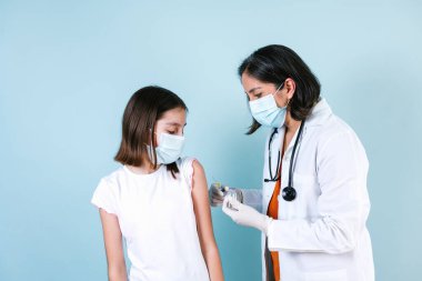 Latin tıp doktoru ya da hemşire mavi stüdyo geçmişi üzerinden İspanyol çocuk kıza Coronavirus aşısı yapıyor.