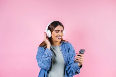 Latin Amerika 'da kulaklıklı, dans eden ve pembe arka planda müzik dinleyen İspanyol genç bir kadın.