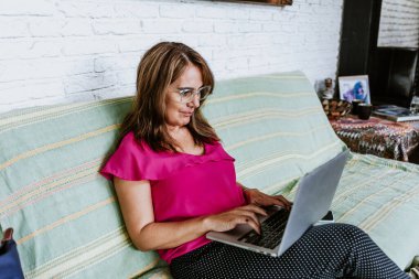 Latin Amerika 'daki ev ofisinin bilgisayarını kullanarak orta yaşlı İspanyol bir kadın evde çalışıyor.