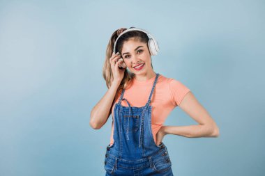 Latin Amerika 'da mavi arka planda, kulaklıklı, dans eden ve müzik dinleyen İspanyol genç bir kadın.