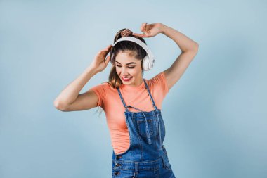 Latin Amerika 'da mavi arka planda, kulaklıklı, dans eden ve müzik dinleyen İspanyol genç bir kadın.