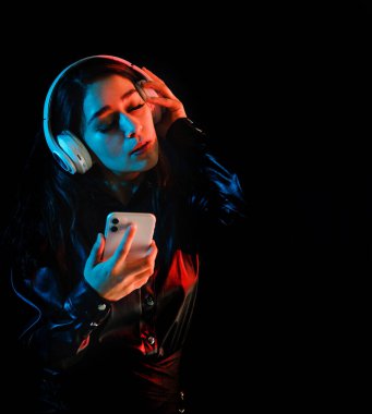 Latin kulaklıklı genç bir kadın Meksika Latin Amerika 'da renkli neon ve siyah arka planda müzik dinliyor.