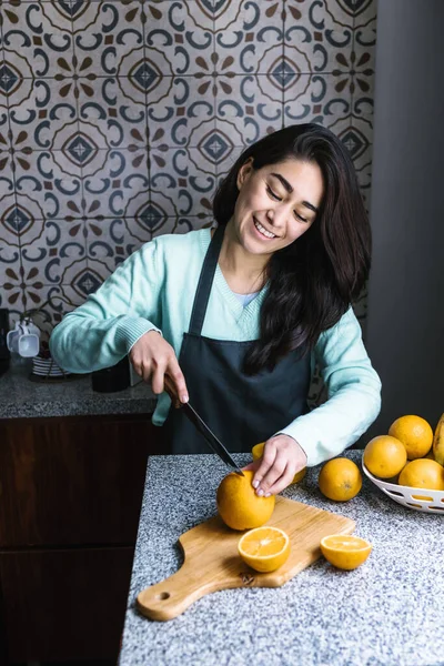 ヒスパニック系の若いですラテン女性準備オレンジジュースでザキッチンでメキシコラテンアメリカ — ストック写真