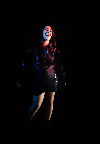 young latin woman dressed in black clothes with colorful red-blue lights on black background in Mexico Latin America