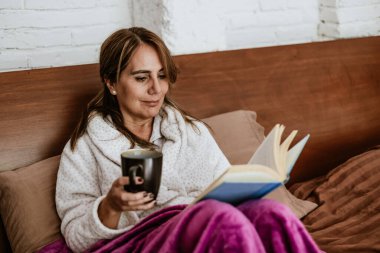 Latin Amerika 'da evde yatakta kitap okuyan son sınıf öğrencisi yetişkin bir kadın.
