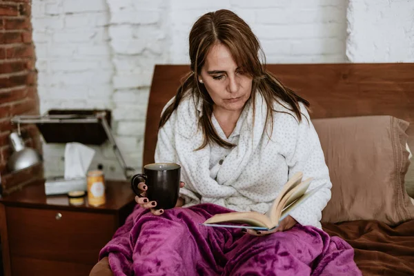 Latin Amerika 'da evde yatakta kitap okuyan son sınıf öğrencisi yetişkin bir kadın.