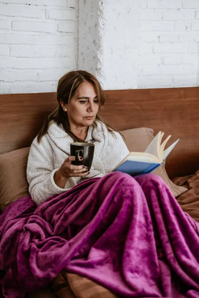 Latin Amerika 'da evde yatakta kitap okuyan son sınıf öğrencisi yetişkin bir kadın.