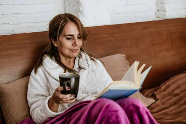 Latin Amerika 'da evde yatakta kitap okuyan son sınıf öğrencisi yetişkin bir kadın.