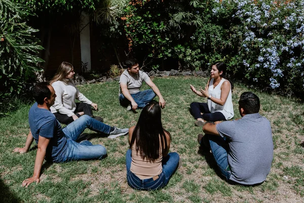 hispanic young people seated in circle on grass and participating at group therapy session or meeting in Mexico Latin America