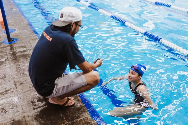 Latin swimming man trainer talking some advices to teenager girl swimmer student at the pool in Mexico Latin America