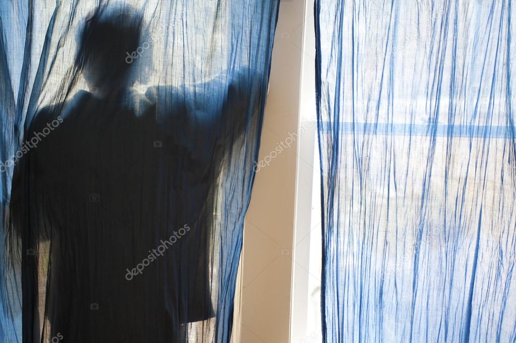 Silhouette of young man against blue curtains