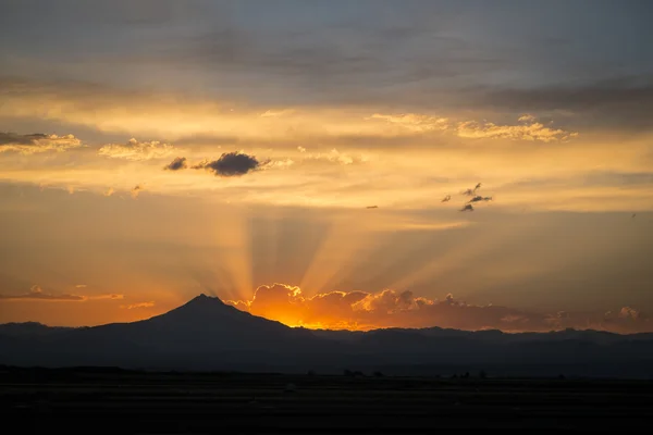 Raios de pôr do sol atrás da silhueta da montanha — Fotografia de Stock