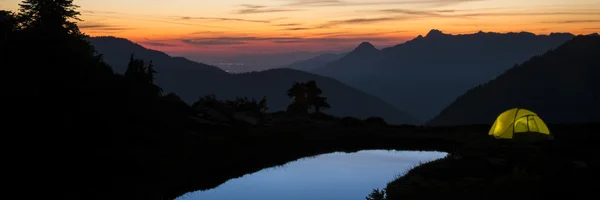 Tent glowing beside blue pond at sunset — Stock Photo, Image