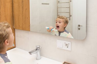 Beş yaşında bir çocuk banyoda ellerini yıkıyor. Beş yaşında, Avrupalı bir çocuk ellerini aynanın önünde banyoda yıkıyor.