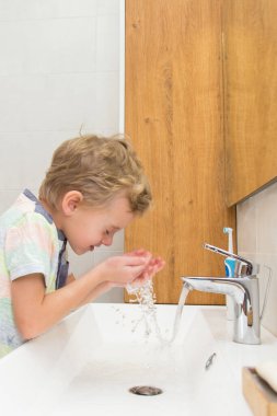 Beş yaşında bir çocuk banyoda ellerini yıkıyor. Beş yaşında, Avrupalı bir çocuk ellerini aynanın önünde banyoda yıkıyor.