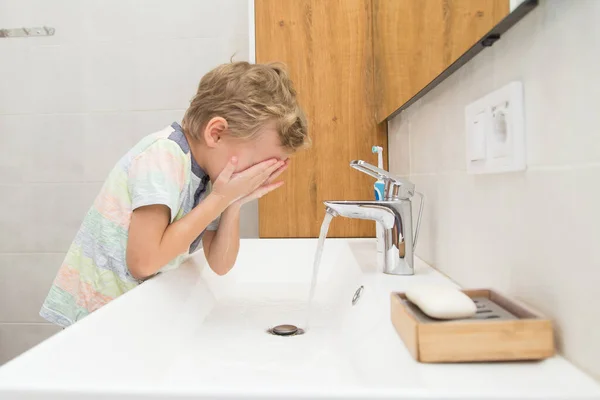 Beş yaşında bir çocuk banyoda ellerini yıkıyor. Beş yaşında, Avrupalı bir çocuk ellerini aynanın önünde banyoda yıkıyor.